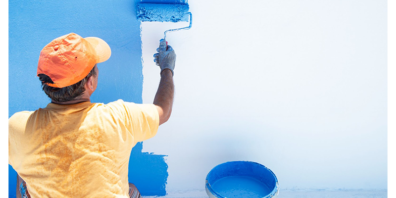 Hombre de espaldas pintando una piscina con pintura celeste.