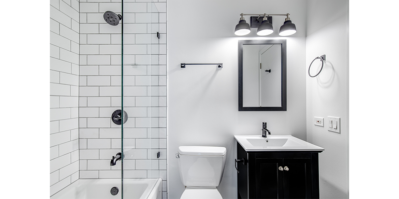 Baño pequeño en blanco y negro con inodoro, vanitory, espejo y ducha.