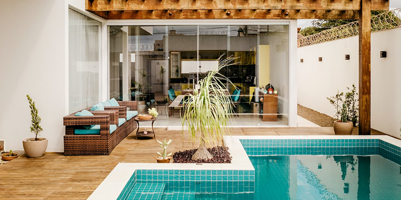 Jardín estilo mediterráneo con piscina, deck de madera, sillones y plantas en macetas.