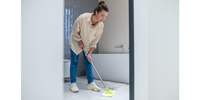 Mujer joven limpiando el piso del baño con mopa.