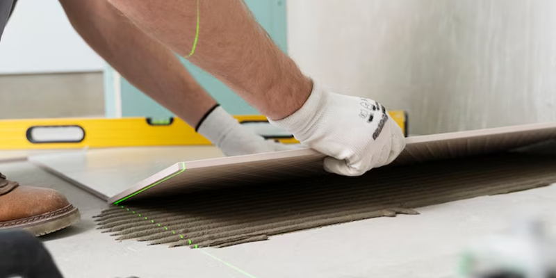 Manos con guantes instalando una pieza de porcelanato.