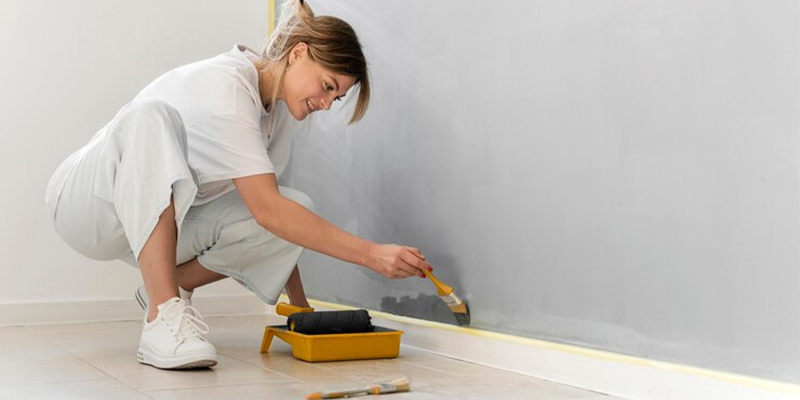 Mujer pintando de gris una pared, usando una brocha.