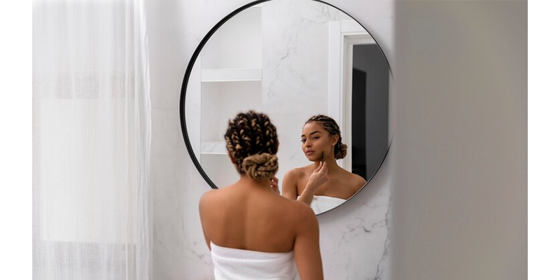 Mujer en el baño frente a un espejo redondo, haciendo skin care.